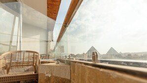Un balcon avec vue sur les pyramides, une chaise en osier et des murs en pierre.