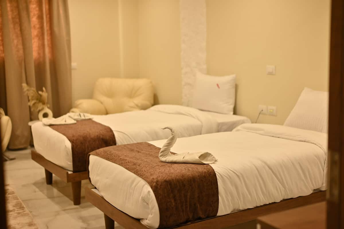 Two single beds with brown headboards and white linens, a beige chair, and a decorative swan towel on one bed.