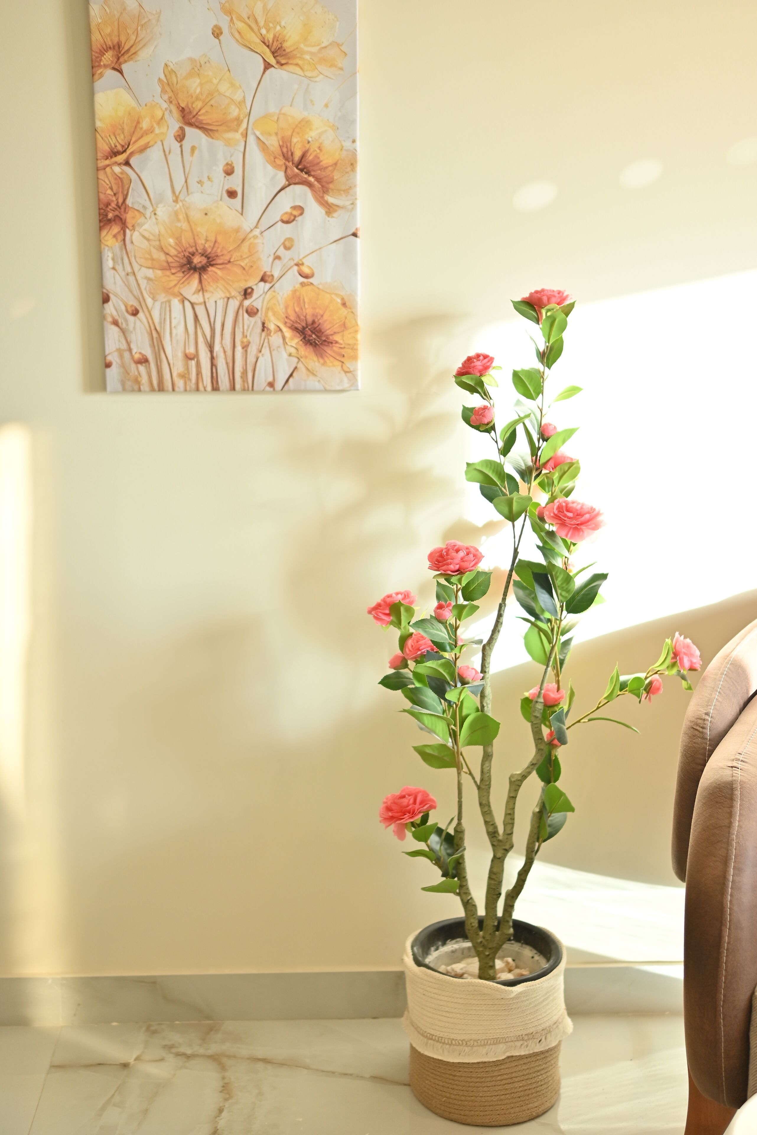 A potted plant with pink flowers on a marble floor, a beige wall, and a painting of yellow flowers.