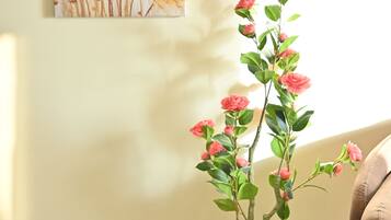 A potted plant with pink flowers on a marble floor, a beige wall, and a painting of yellow flowers.