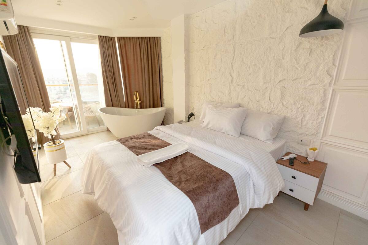 A bedroom with a large bed, a bathtub, and a nightstand with a lamp.