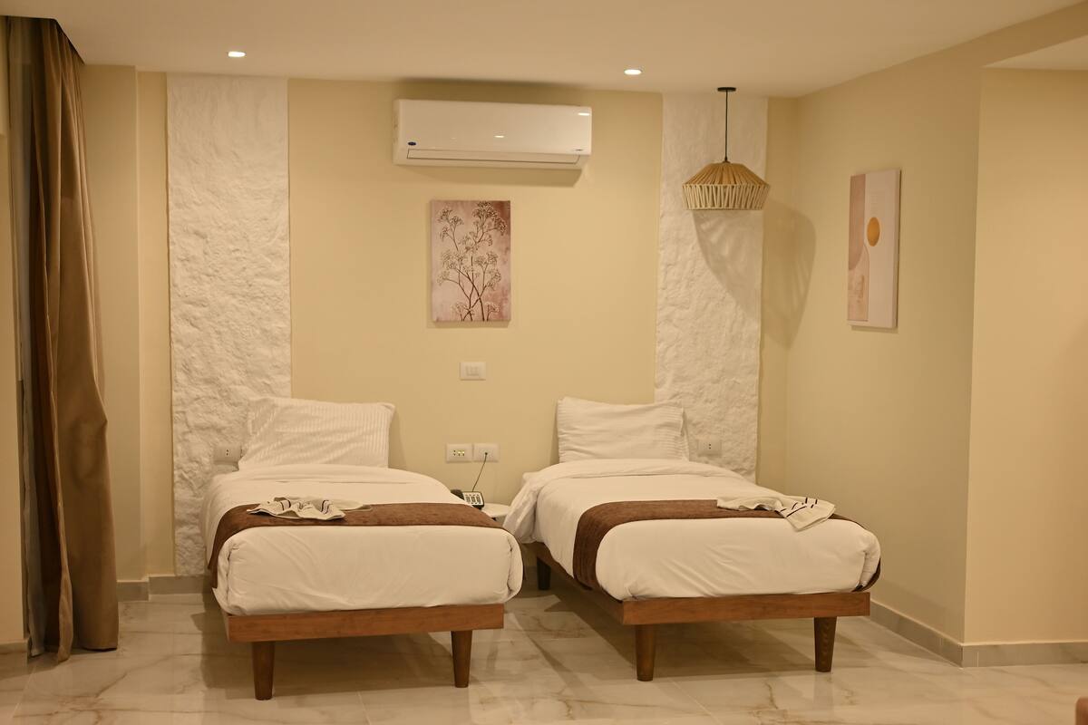 A hotel room with two beds, a marble floor, an air conditioning unit, and artwork on the walls.