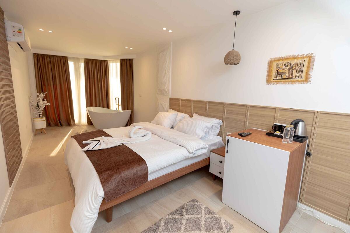A hotel room with a bed, bedside table, and a small desk with a kettle.