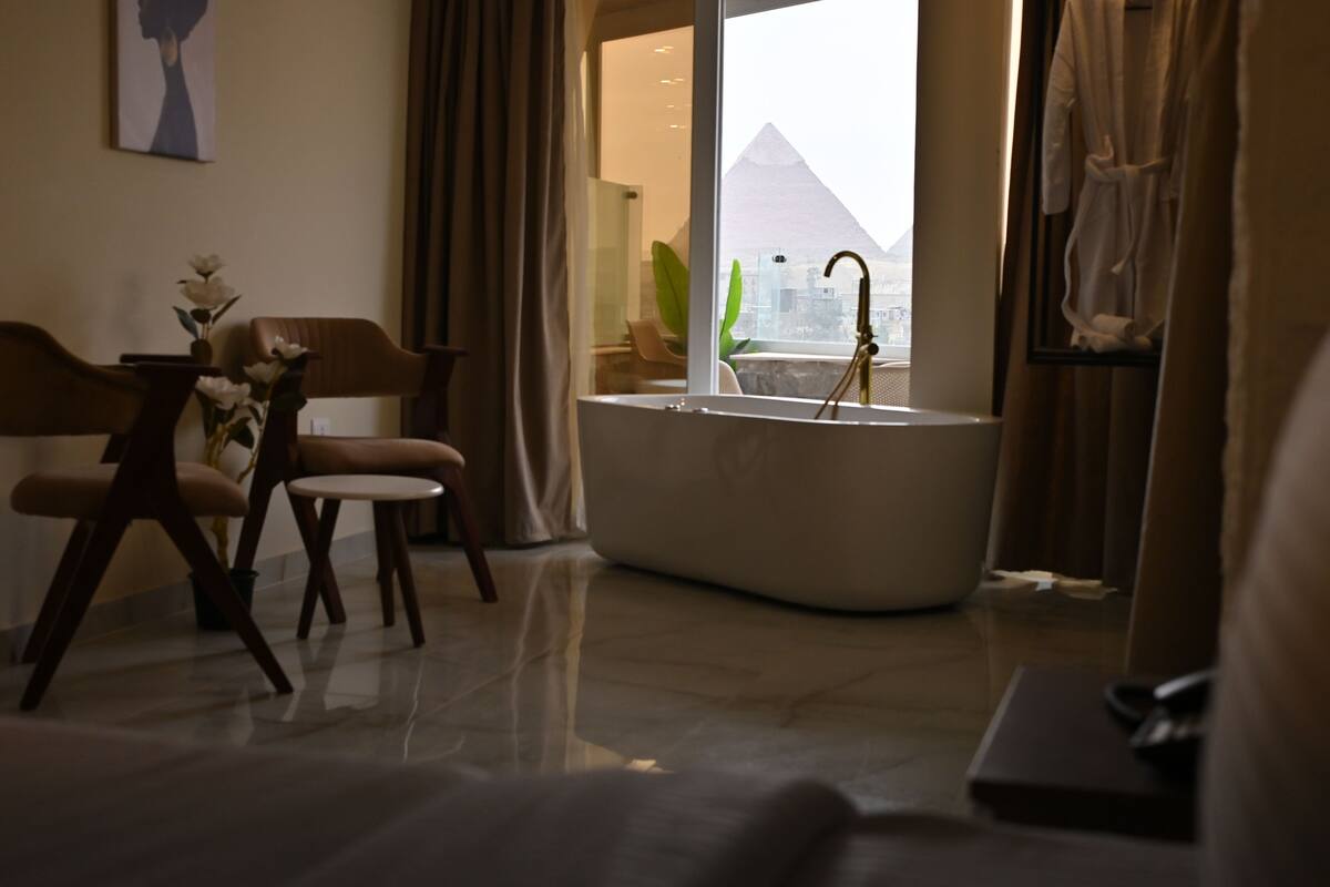 A modern living room with a large bathtub, a dining area with chairs, and a view of the pyramid.