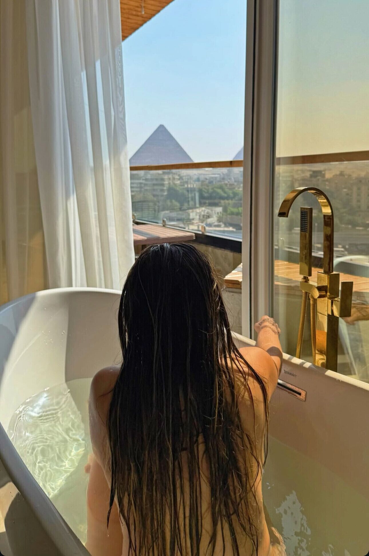A person in a bathtub with a view of a pyramid and buildings.