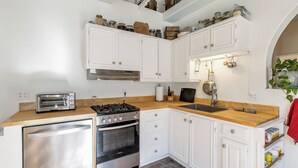 A compact kitchen with white cabinets, a stainless steel refrigerator, a gas stove, and a sink.