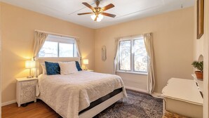 A bedroom with a bed, nightstands, a ceiling fan, and two windows with curtains.