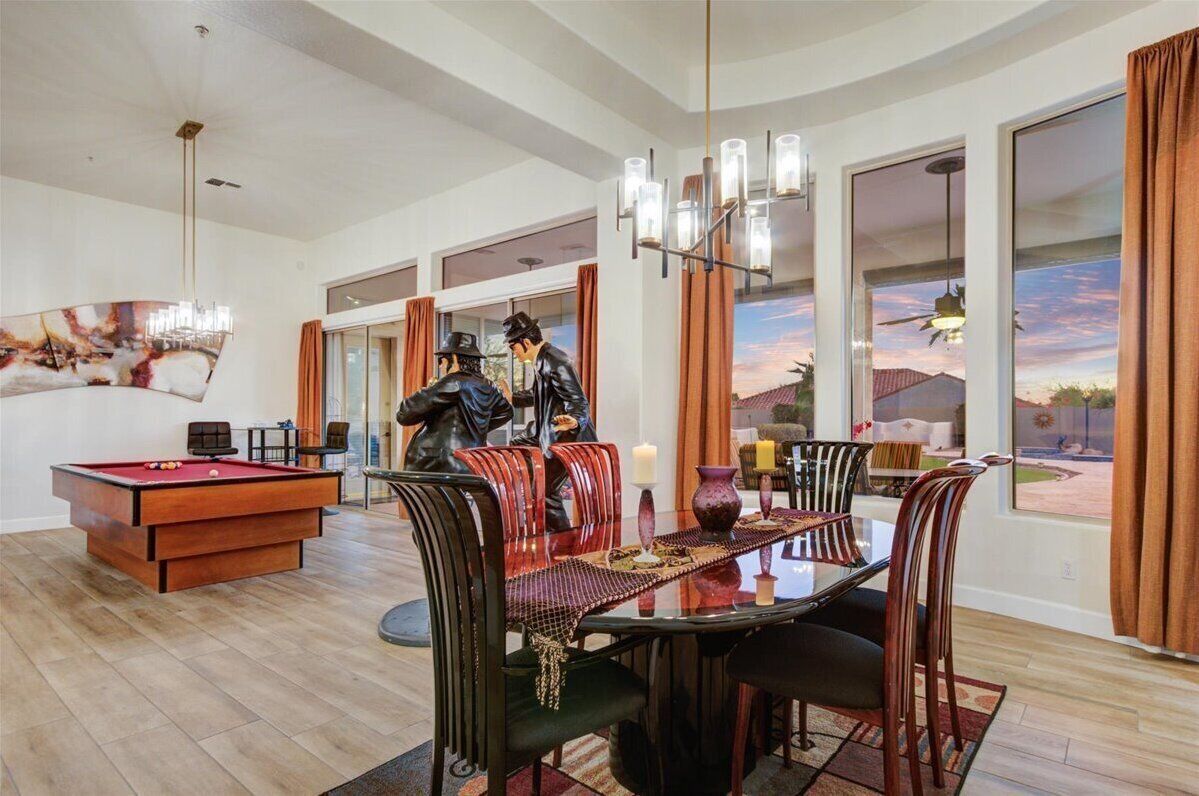 A spacious living area with a pool table, a dining table with chairs, and a large window offering a view of the outdoors.
