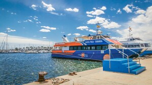 Un ferry atracado en un puerto deportivo, con cielo despejado y varios barcos al fondo.