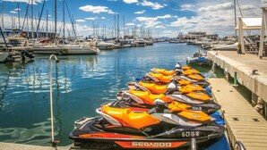Un puerto deportivo con varias embarcaciones amarradas y una hilera de motos acuáticas en el muelle.