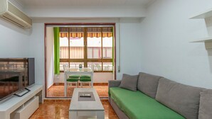 Una sala de estar con televisor, un sofá, una mesa de comedor con sillas y una ventana con cortinas.