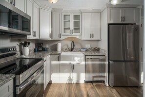 A modern kitchen with stainless steel appliances, white cabinetry, and a granite countertop.