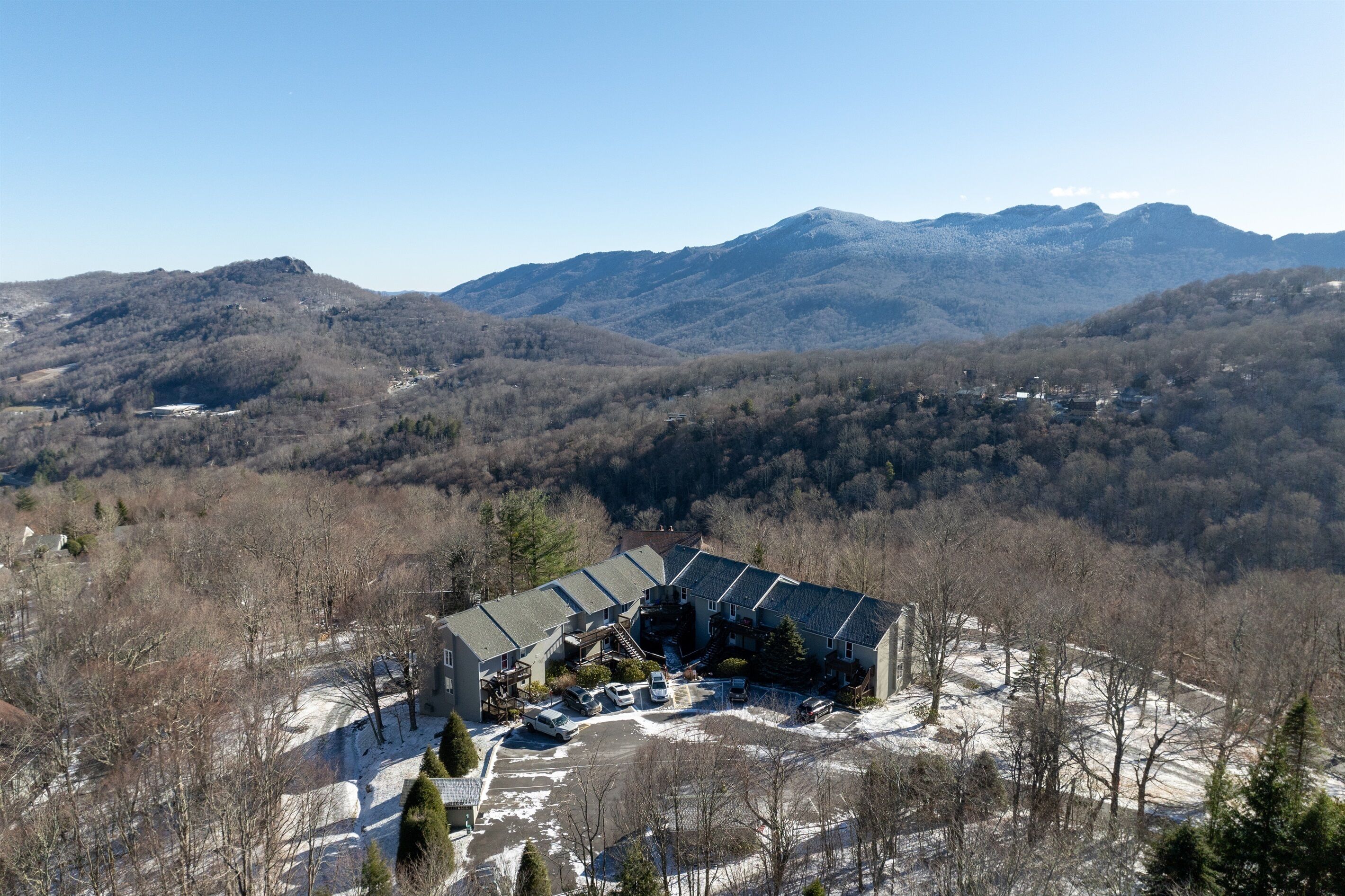 A mountain lodge with a large parking area, surrounded by forested hills and mountains.