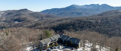 A mountain lodge with a large parking area, surrounded by forested hills and mountains.
