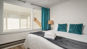 Ein ordentlich bezogenes Bett mit weißer und dunkelgrauer Bettwäsche, türkisfarbenen Kissen und einer Lampe auf dem Nachttisch.