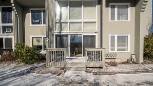 Ein mehrstöckiges Wohngebäude mit Hauseingang, überdachter Veranda und einem kleinen Garten, der mit Schnee bedeckt ist.