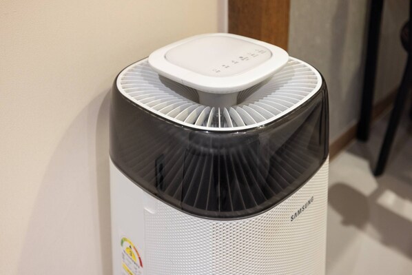 Un purificador de aire Samsung blanco con pantalla digital en la parte superior, colocado contra una pared.