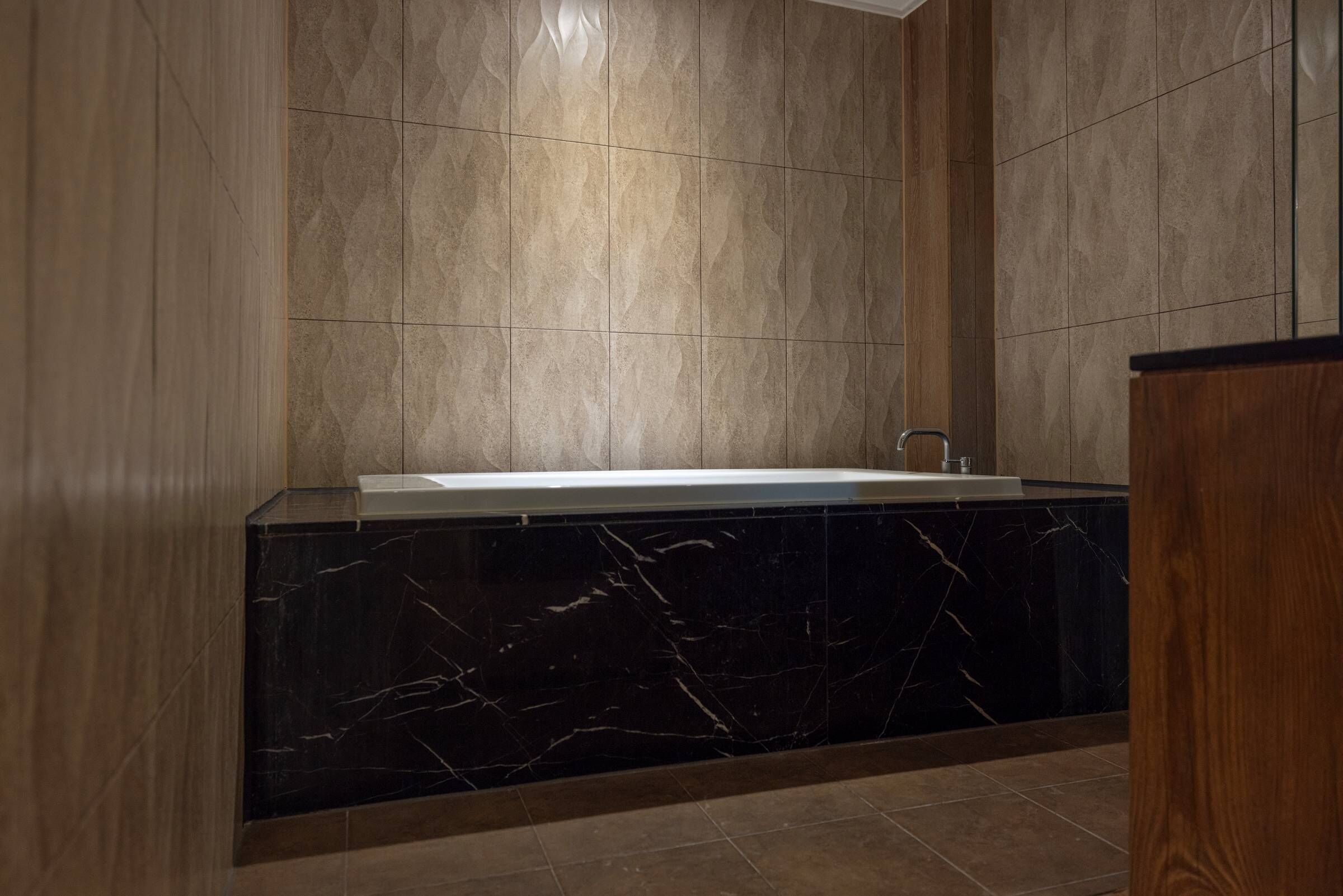A modern bathroom with a marble bathtub, wooden paneling, and a tiled wall.