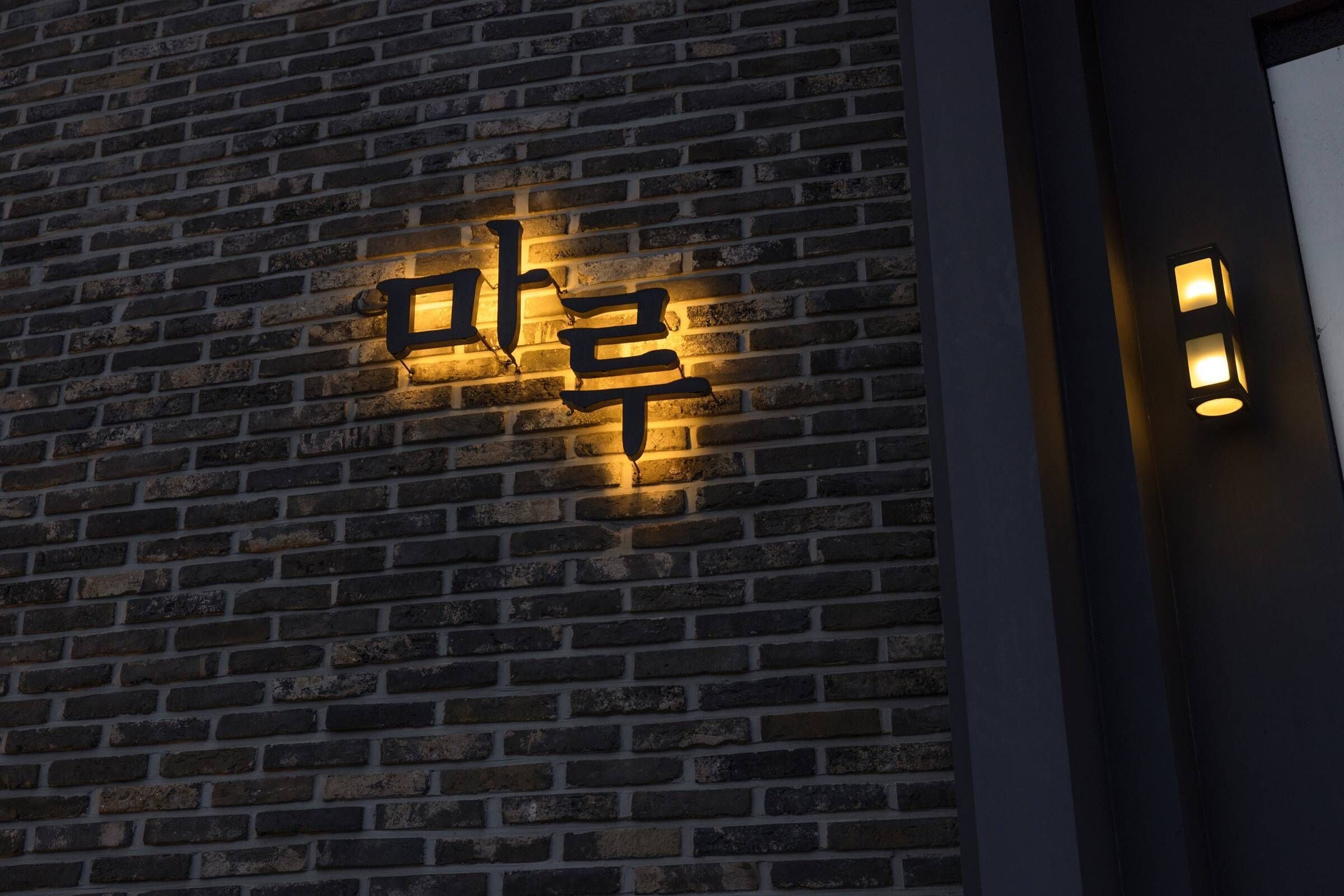 Pared de ladrillo con caracteres coreanos iluminados, indicando un lugar en Corea.