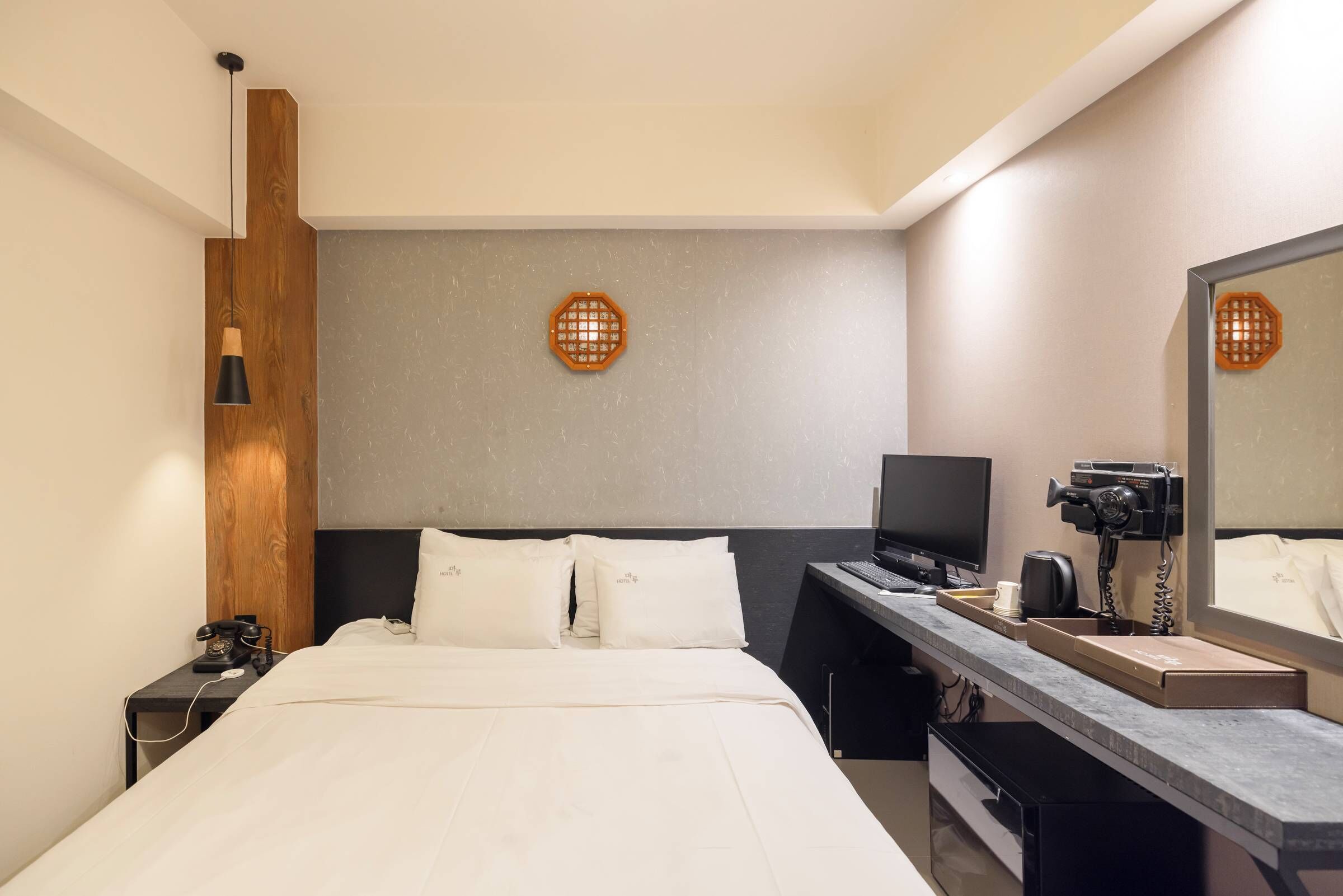 Quarto de hotel moderno com cama, escrivaninha, computador, telefone e espelho.