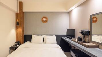 Quarto de hotel moderno com cama, escrivaninha, computador, telefone e espelho.