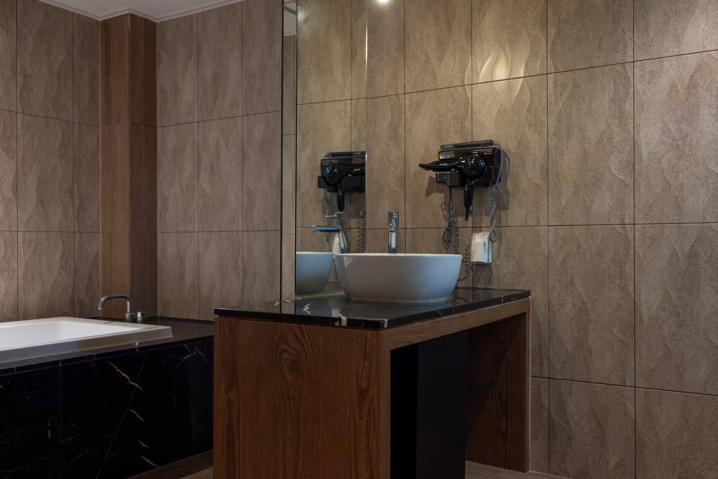 Un baño moderno con un lavamanos de mármol, un espejo grande y un secador de pelo fijado a la pared.