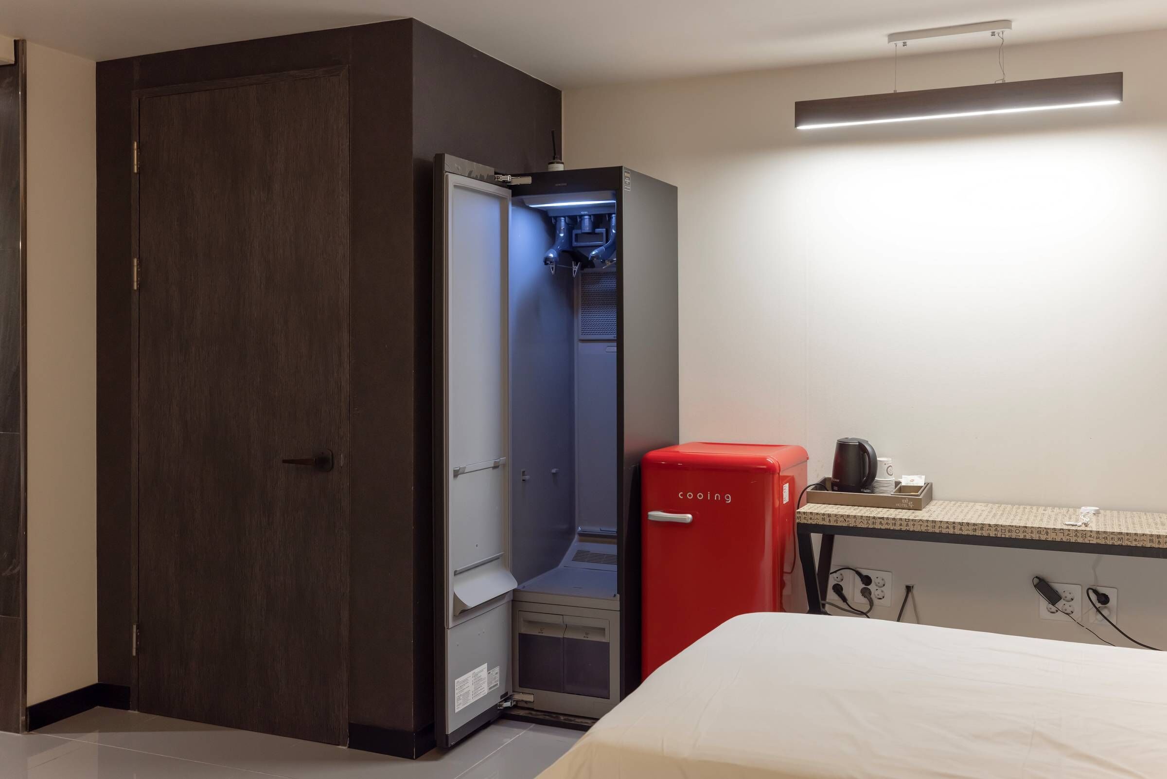 Ein kleines Hotelzimmer mit Kleiderschrank, einer roten Minibar und einem Bett.