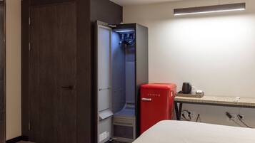 Ein kleines Hotelzimmer mit Kleiderschrank, einer roten Minibar und einem Bett.