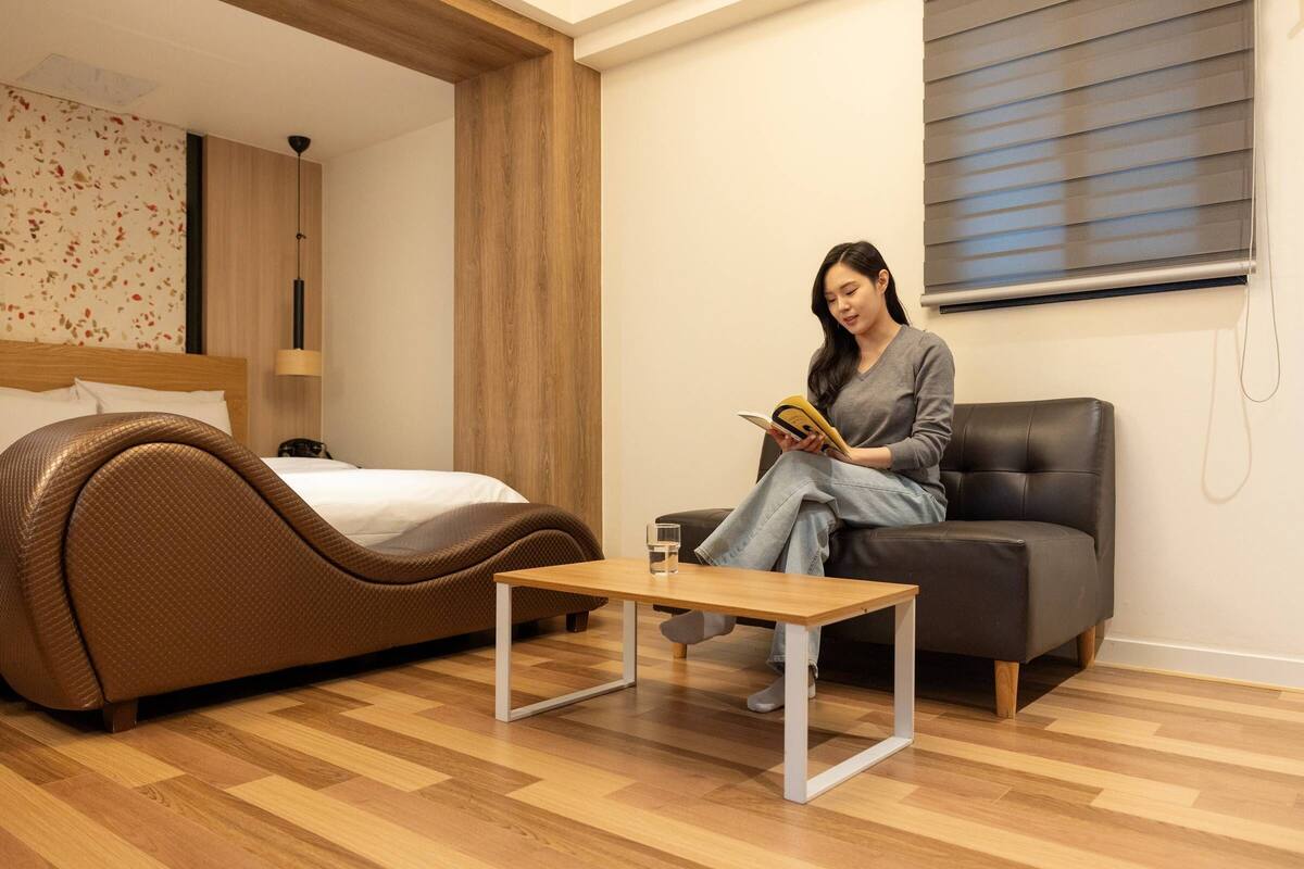 Une chambre moderne avec un canapé aux lignes courbes, une table basse en bois et un lit doté d’une tête de lit.