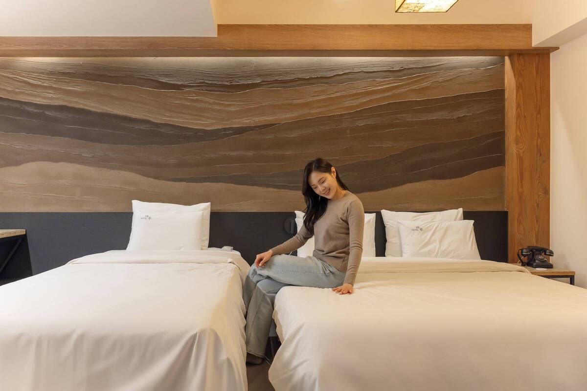 Une chambre d’hôtel avec deux lits, une tête de lit en bois et un téléphone sur une table de chevet.