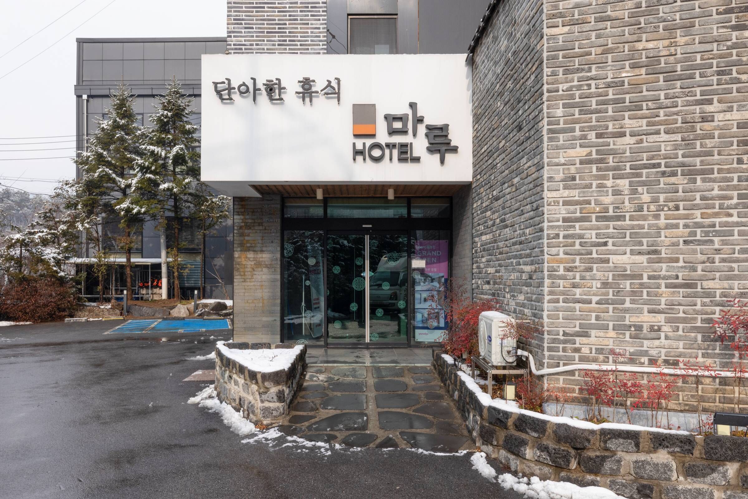 A hotel entrance with a modern facade, stone steps leading up to the entrance, and a snow-covered ground.