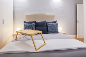 Ein Bett mit Nachttisch aus Holz, zwei Nachttischlampen und einem Kopfteil mit vielen Kissen.