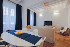 Ein Zimmer mit Esstisch, Stühlen, einer Couch, einem Fernseher und einem Fenster mit Vorhängen.