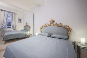 Un dormitorio con una cama grande, un espejo, una mesita de noche y una ventana con cortinas.