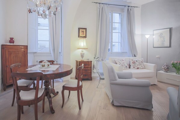 A dining area with a wooden table and chairs, a white sofa, and a chandelier.