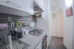 A modern kitchen with a gas stove, hanging utensils, and a clock on the wall.