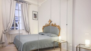 Ein Schlafzimmer mit einem Bett, einem Nachttisch mit Lampe, einem Fenster mit Vorhängen und einer Heizung.