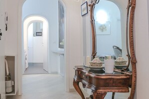 A hallway with a mirror, a wooden table with decorative items, and a door leading to another room.