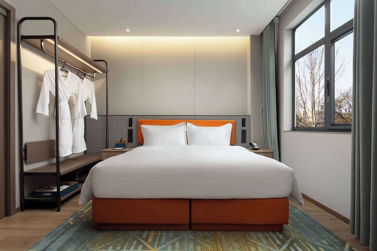 A modern hotel room with a large bed, a built-in wardrobe, and a view of trees through the window.