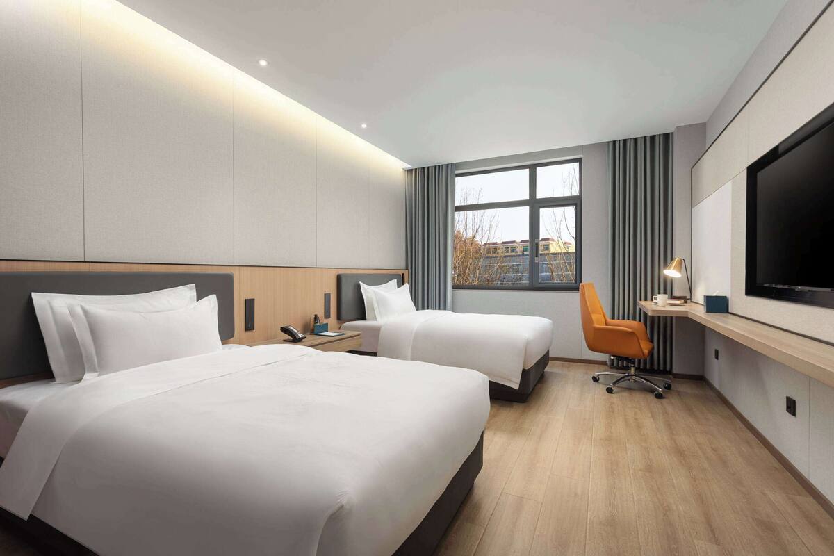 A hotel room with two beds, a desk, a TV, and a window with curtains.