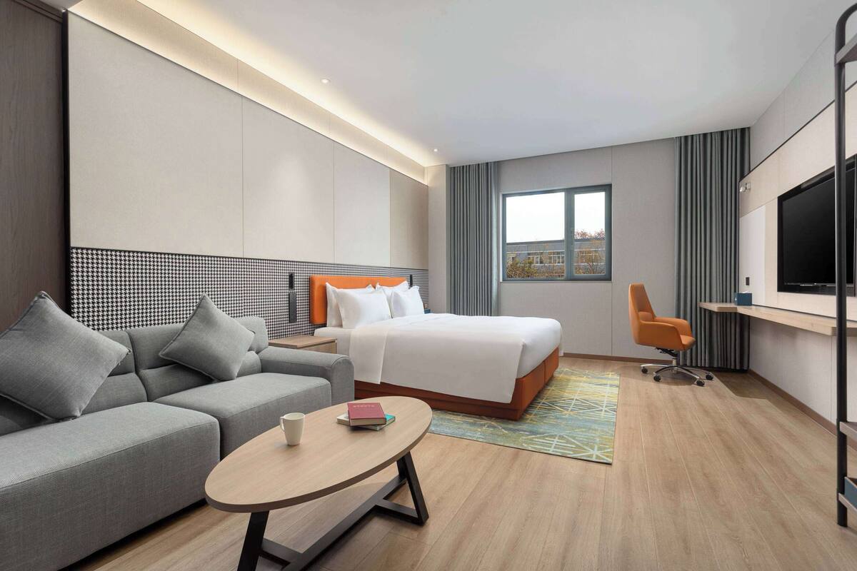 A modern hotel room with a sofa, bed, TV, and a small table.