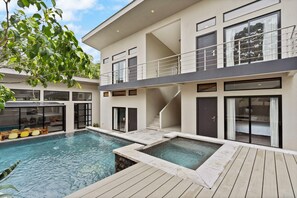 Una moderna casa a due piani con piscina, terrazza in legno e una scala che conduce al piano superiore.