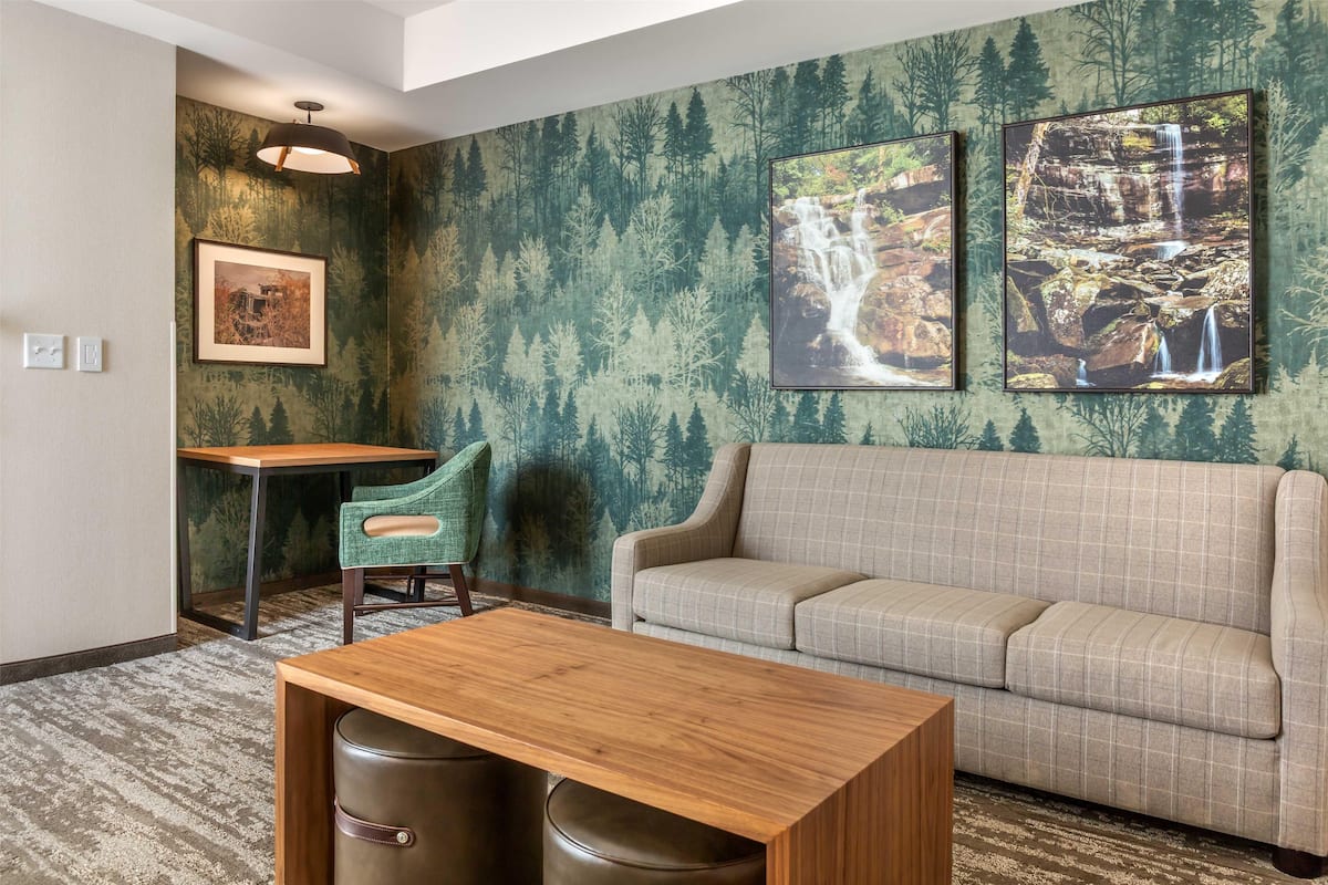A room with a sofa, a table, and a chair. There are two framed pictures on the wall.