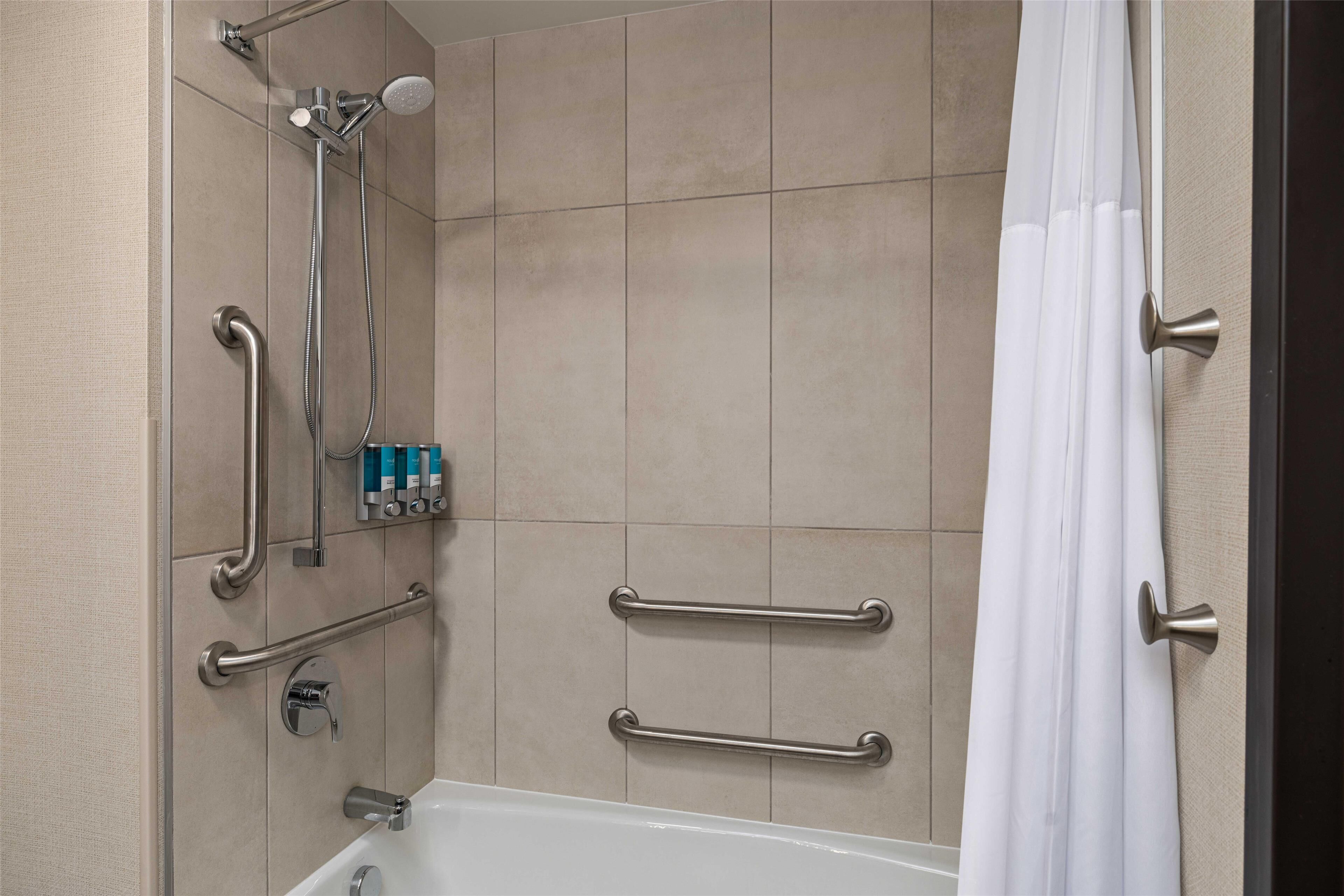 A bathroom with a bathtub, a shower with a handheld showerhead, and grab bars.