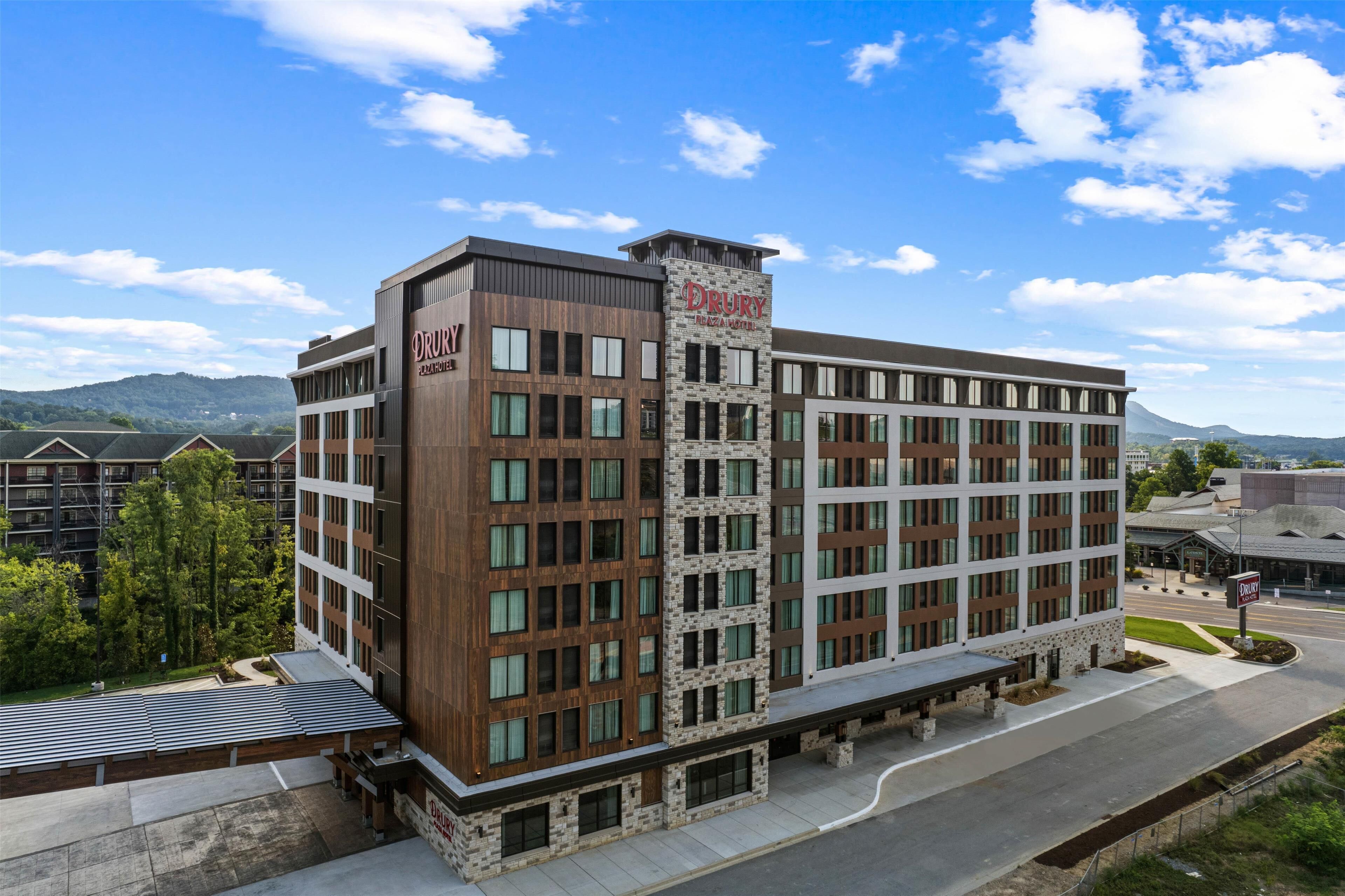 Un hôtel à plusieurs étages, reconnaissable à son grand panneau « Drury », qui présente une architecture moderne avec une combinaison de façades en bois et en pierre, et qui dispose d’un parking à l’avant.