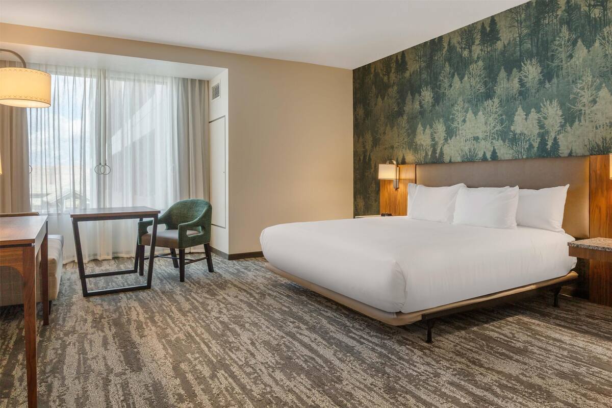 A hotel room with a large bed, a desk, a chair, and a window with curtains.