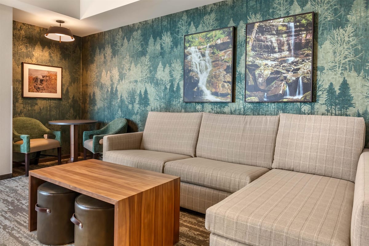 A modern living room with a sectional sofa, a wooden coffee table, and two trash bins. There are framed pictures on the wall and a small round table.