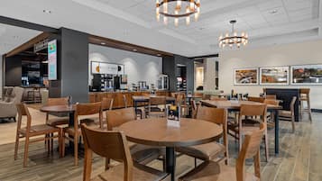 A modern restaurant with round tables and wooden chairs, a bar area, and a visible menu board.