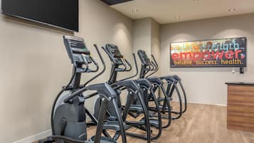 A gym with four treadmills lined up against a wall, a motivational poster, and a reception desk.