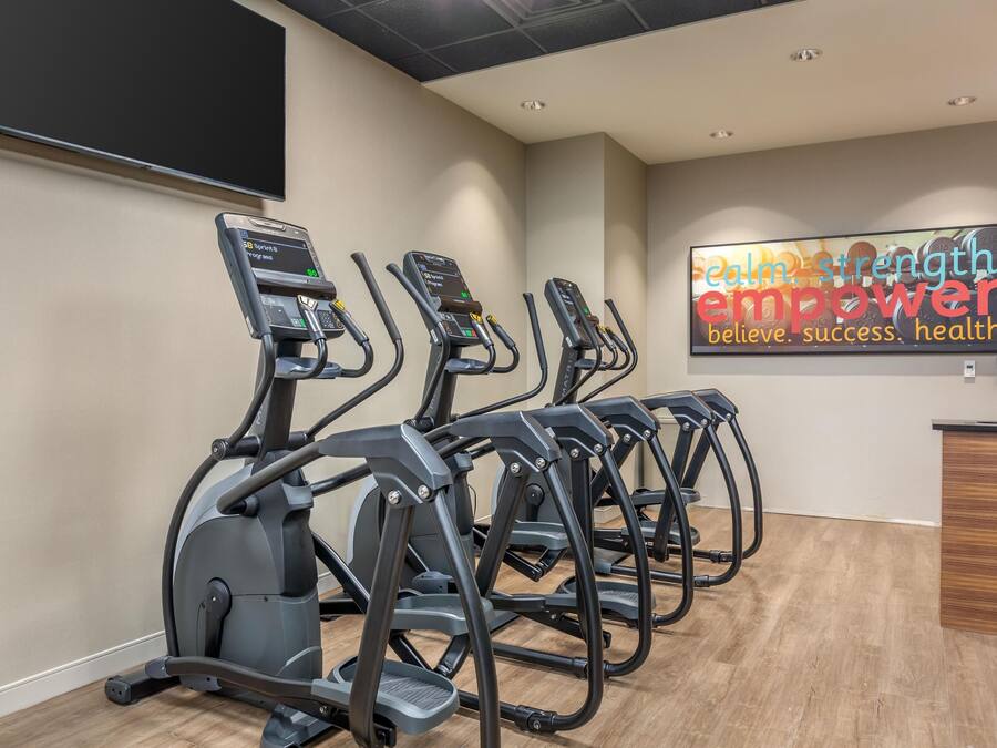 A gym with four treadmills lined up against a wall, a motivational poster, and a reception desk.